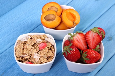 Fresh strawberries and apricots, wheat and rye flakes in glass bowl on blue boards, concept of...