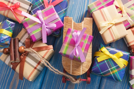 Wooden sled and wrapped colorful gifts with ribbons for Christmas or other celebration lying on old boardsの写真素材