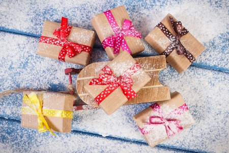 Wooden sled and wrapped gifts with colorful ribbons for Christmas, Valentine, birthday or other celebration lying on snowy boardsの写真素材