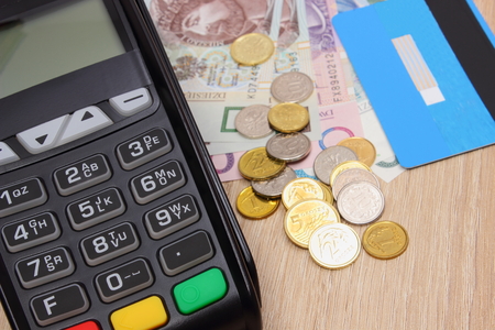 Payment terminal with credit card and polish currency money on wooden desk, paying using credit card or cash, finance and banking conceptの写真素材