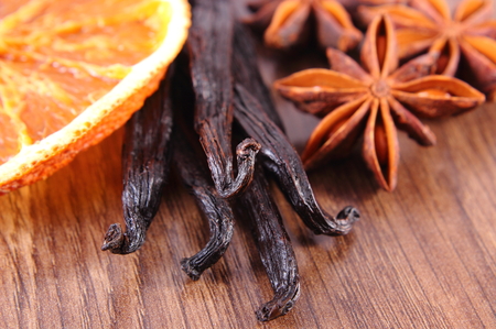 Fresh fragrant vanilla sticks pods, star anise and slices of dried orange on wooden board, seasoning...
