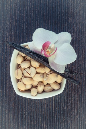 Vintage photo, Pistachio nuts in white bowl, colorful blooming orchid flower and fresh fragrant vanilla sticks pods, cosmetics ingredientsの写真素材