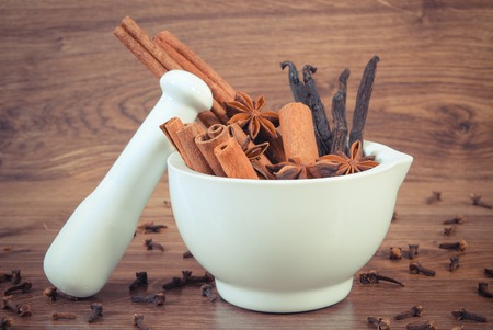 Vintage photo, fragrant anise, cinnamon and vanilla sticks in white glass mortar and cloves on rustic boardの写真素材