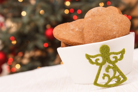 Fresh homemade gingerbreads in white bowl and christmas tree with lights in backgroundの写真素材