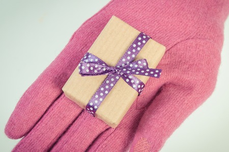 Vintage photo, Hand of woman in pink woolen gloves and wrapped gift for Christmas, Valentine, birthday or other celebration, white backgroundの写真素材