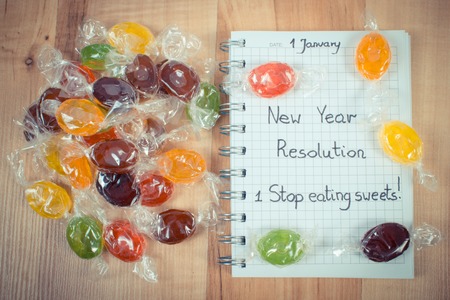 Vintage photo, New years resolutions stop eating sweets written in notebook and colorful candies,...