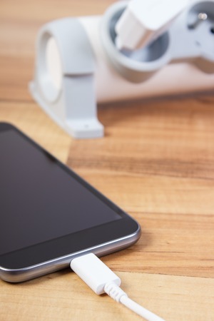 Mobile phone with connected plug of charger, smartphone charging on tableの写真素材