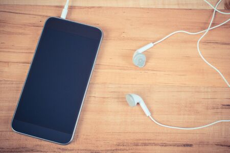 Vintage photo, Mobile phone, smartphone with headphones on wooden tableの写真素材