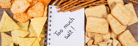 Inscription too much salt in notebook, crunchy potato crisps, breadsticks and cookies, concept of restriction eating unhealthy and salted foodの写真素材
