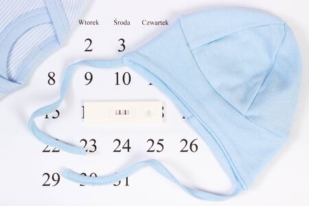 Pregnancy test with positive result and clothing for newborn on calendar with polish inscription, concept of extending family and expecting for babyの写真素材