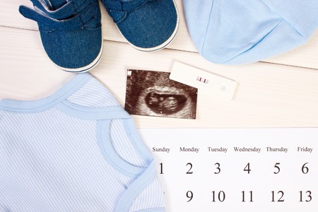 Pregnancy test with positive result, ultrasound scan of baby, clothing for newborn and calendar, concept of extending family and expecting for babyの写真素材