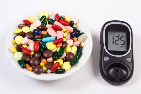 Glucose meter with result of measurement sugar level and heap of colorful medical pills, capsules or...