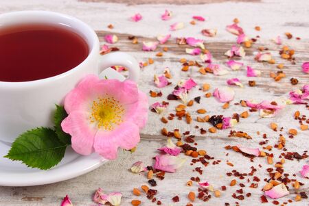 Cup of hot tea with wild rose, fresh blooming flowers and dried petals with tea grains on old wooden backgroundの写真素材
