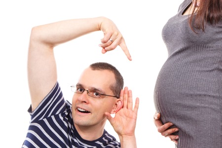Happy father listening and showing belly of his pregnant wife, concept of extending family and expecting for newbornの写真素材