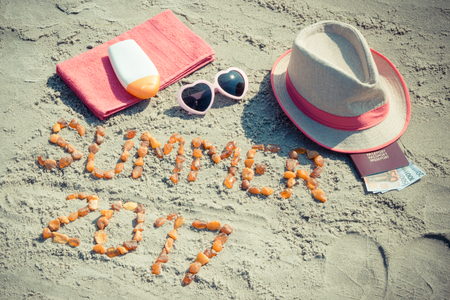 Vintage photo, Inscription summer 2017 made of amber stones, accessories for sunbathing and passport with currencies euro on sand at beach, concept of sunbathing, travel and vacation timeの写真素材