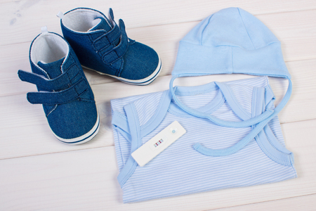Pregnancy test with positive result and clothing for newborn on boards, concept of extending family and expecting for babyの写真素材
