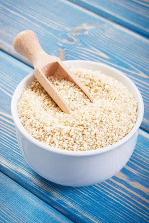 Heap of sesame seeds with wooden scoop in white glass bowl on boards, concept of healthy nutritionの写真素材