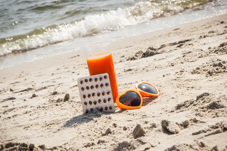 Medical pills, carrot juice and sunglasses on sand at beach, concept of prevention of vitamin A deficiency, beautiful and lasting tanの写真素材