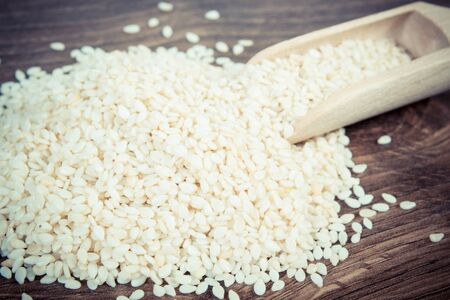 Vintage photo, Heap of sesame seeds with wooden scoop on board, concept of healthy nutritionの写真素材