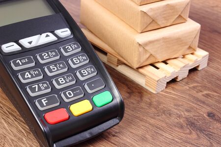Payment terminal and small wrapped boxes on wooden pallet, concept of cashless paying for products and shippingの写真素材