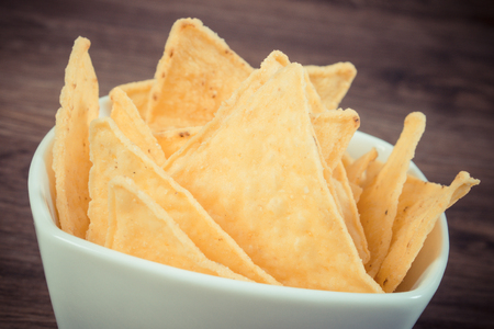 Vintage photo, Heap of crunchy potato crisps in white glass bowl on rustic board, concept of restriction eating unhealthy and salted foodの写真素材