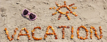 Word vacation, shape of sun made of amber stones and sunglasses at beach, concept of sunbathing and summer timeの写真素材