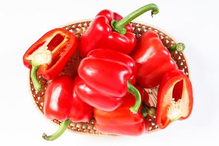 Heap of red peppers in wicker basket lying on white background, concept of healthy nutritionの写真素材