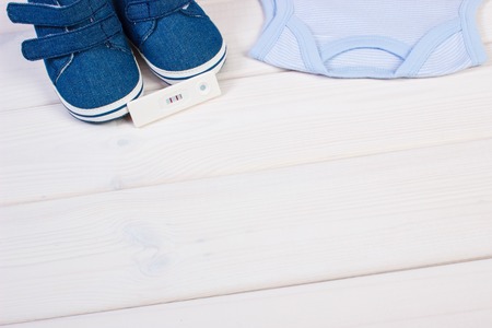 Pregnancy test with positive result and clothing for newborn, concept of extending family and...