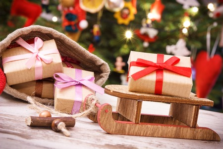 Gifts with ribbon for Christmas on wooden sled and in jute bag on background of christmas tree with lights and decorationの写真素材