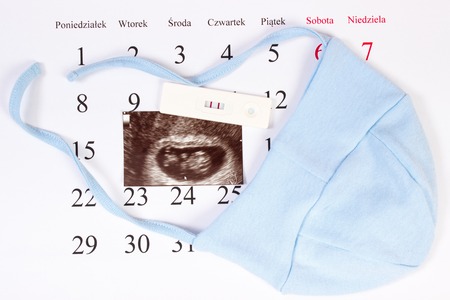 Pregnancy test with positive result, ultrasound scan of baby and clothing for newborn on calendar with polish inscription days, concept of extending family and expecting for babyの写真素材