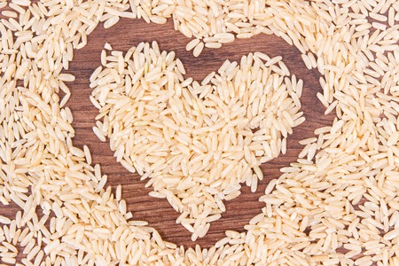 Heap of brown rice in shape of heart on rustic board, concept of healthy nutritionの写真素材