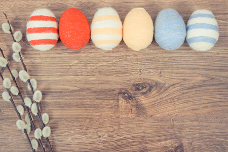 Vintage photo, Twigs of willow and colorful Easter eggs wrapped woolen string on rustic board, festive decoration concept, copy space for textの写真素材