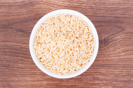 Heap of brown rice in glass bowl on rustic board, concept of healthy nutritionの写真素材