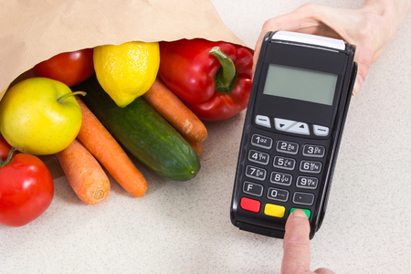 Hand of elderly senior woman using payment terminal, enter personal identification number, paying for shopping, fruits and vegetablesの写真素材