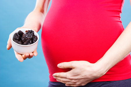 Woman in pregnant holding portion of dried plum in glass bowl, concept of healthy nutrition and vitamin during pregnancyの写真素材