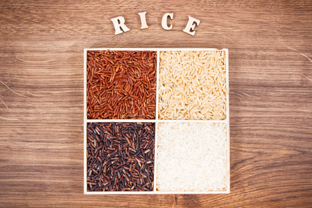 Heap of white, brown, red and black rice with inscription on rustic board, concept of healthy nutritionの写真素材