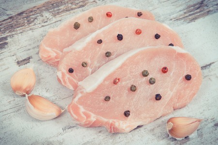 Slices of fresh raw loin with pepper and cloves garlic for cooking lying on old rustic boardの写真素材