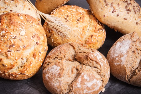 Fresh baked homemade wholegrain rolls with seeds and ears of rye or wheat grainの写真素材