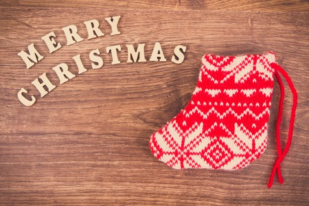Inscription Merry Christmas with festive red woolen sock for gifts on rustic board. Vintage photo