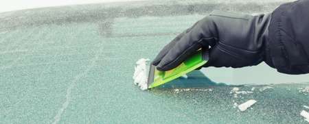Hand in black leather glove scraping ice or snow from car windscreen, winter problems in transportation conceptの写真素材