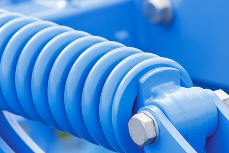 Steel spring as detail of blue industrial or agricultural machinery, part of hydraulic or pneumatic equipments, engineering and technology conceptの写真素材