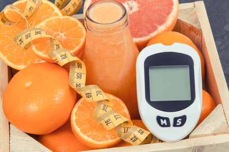 Glucose meter for measuring sugar level, freshly blended coctail from citrus fruits and centimeter. Diabetes, slimming, diet and healthy nutrition conceptの写真素材