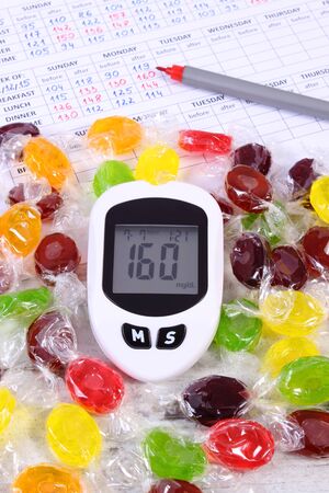Glucometer, pen and colorful candies on medical form with result of measurement sugar level, checking and measuring sugar levelの写真素材