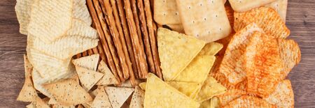 Heap of crunchy potato crisps, breadsticks and cookies on rustic board, concept of restriction...