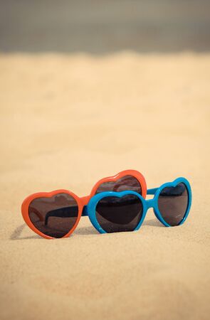 Blue and red sunglasses in shape of heart on sand at beach. Summer time and vacation conceptの写真素材