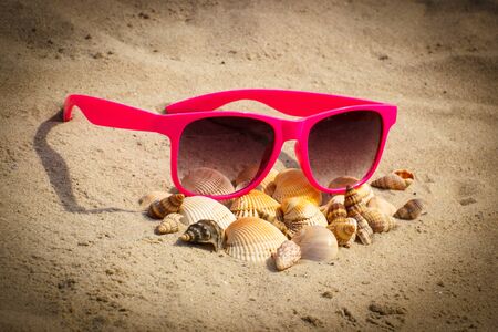 Heap of shells and pink sunglasses lying on sand at beach, vacation and summer time, eye protectionの写真素材