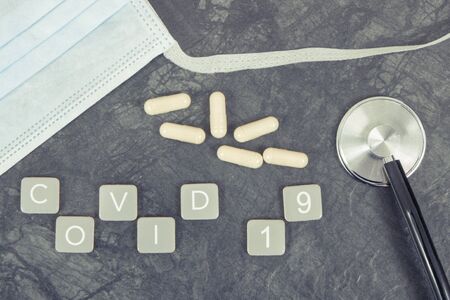 Inscription covid 19 with surgical or protective mask, tablets and stethoscope.の写真素材