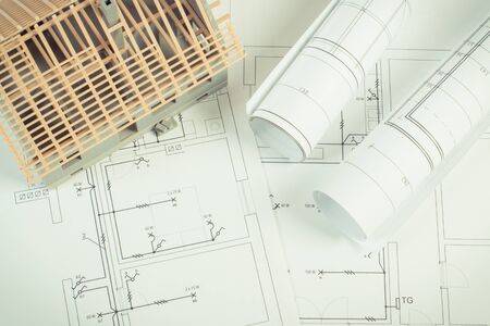 Small house under construction and electrical rolls of diagrams and drawings for project, concept of...
