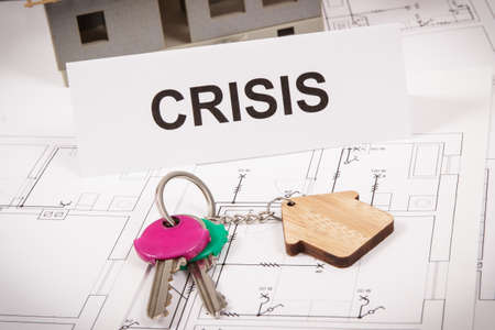 Keys with house shape and inscription crisis on housing plan. Fall and crisis of real estate market. Reduced housing pricesの写真素材