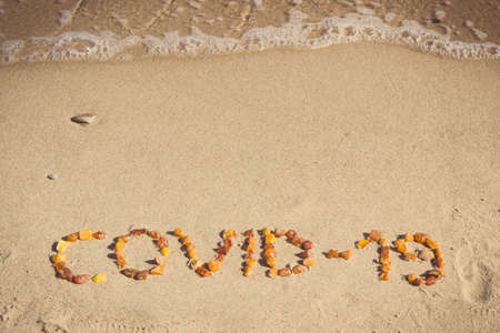 Inscription Covid-19 made of amber stones on sand at beach. Holidays, safe and protection during...